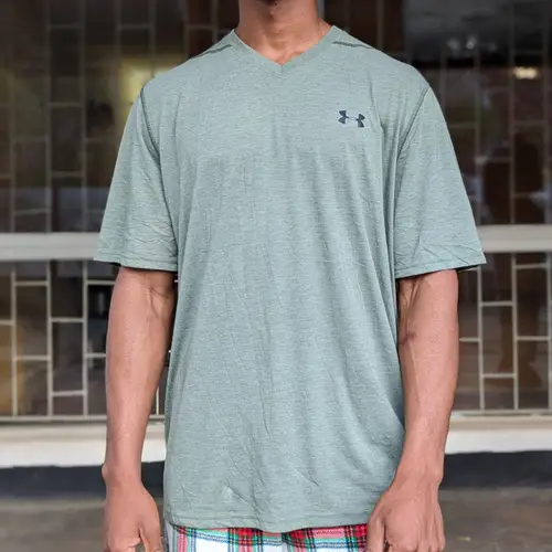 A man wearing a green v-neck t-shirt with plaid shorts.