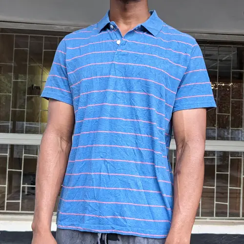 A man wearing a blue polo shirt with pink stripes, standing outdoors.