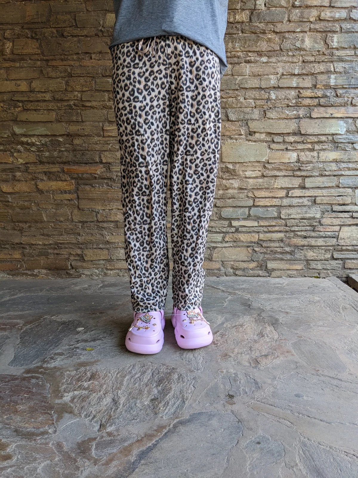 A person wearing leopard print lounge pants and pink shoes.