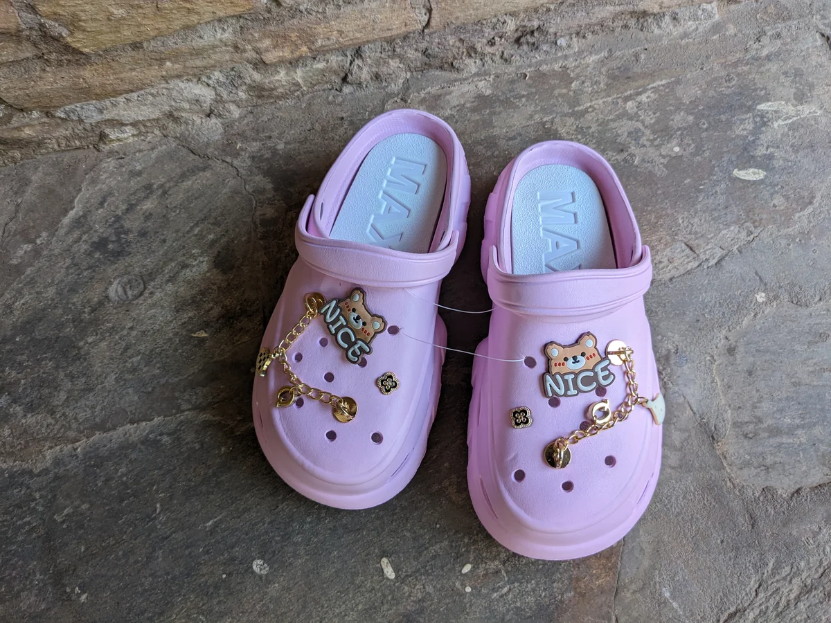 A pair of cute pink clogs with character designs and embellishments.