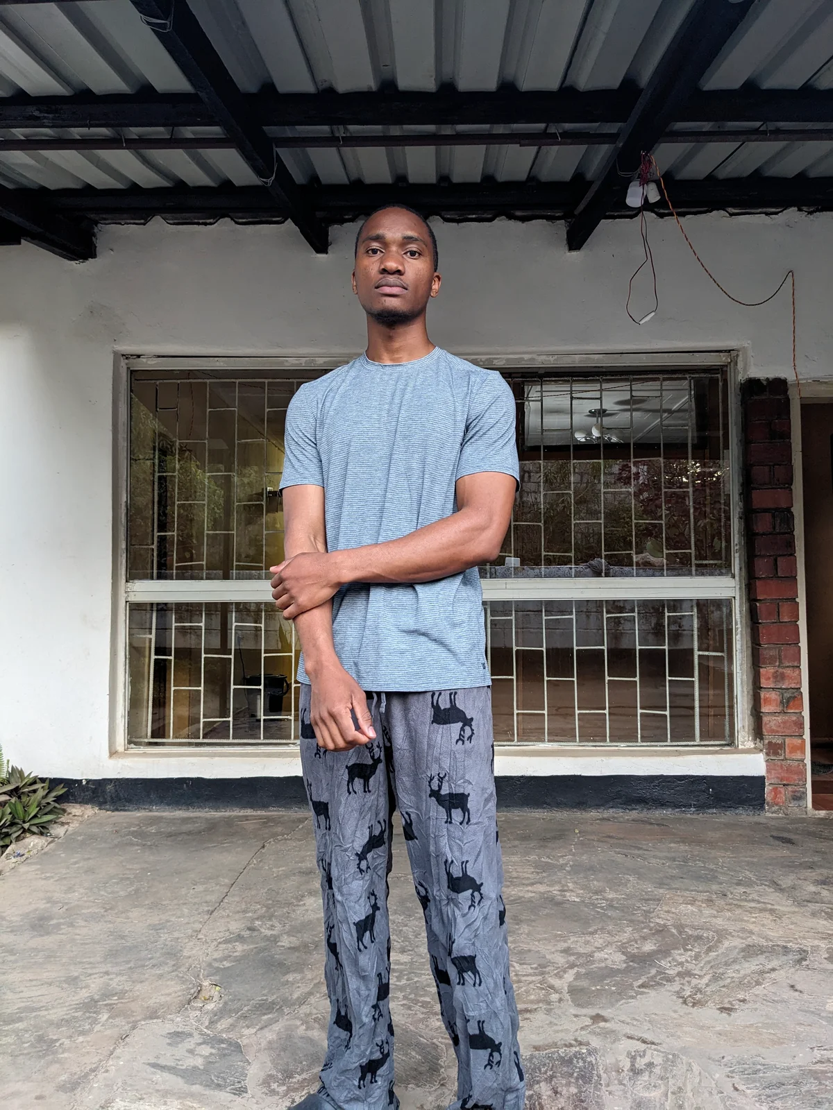 A man wearing a light blue t-shirt and patterned pants standing outdoors.