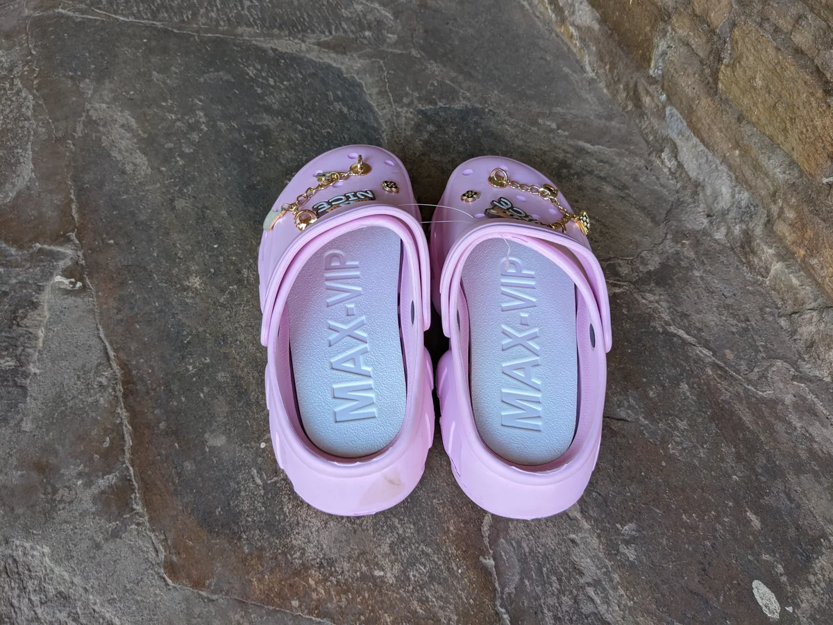A pair of cute pink clogs with character designs and embellishments.