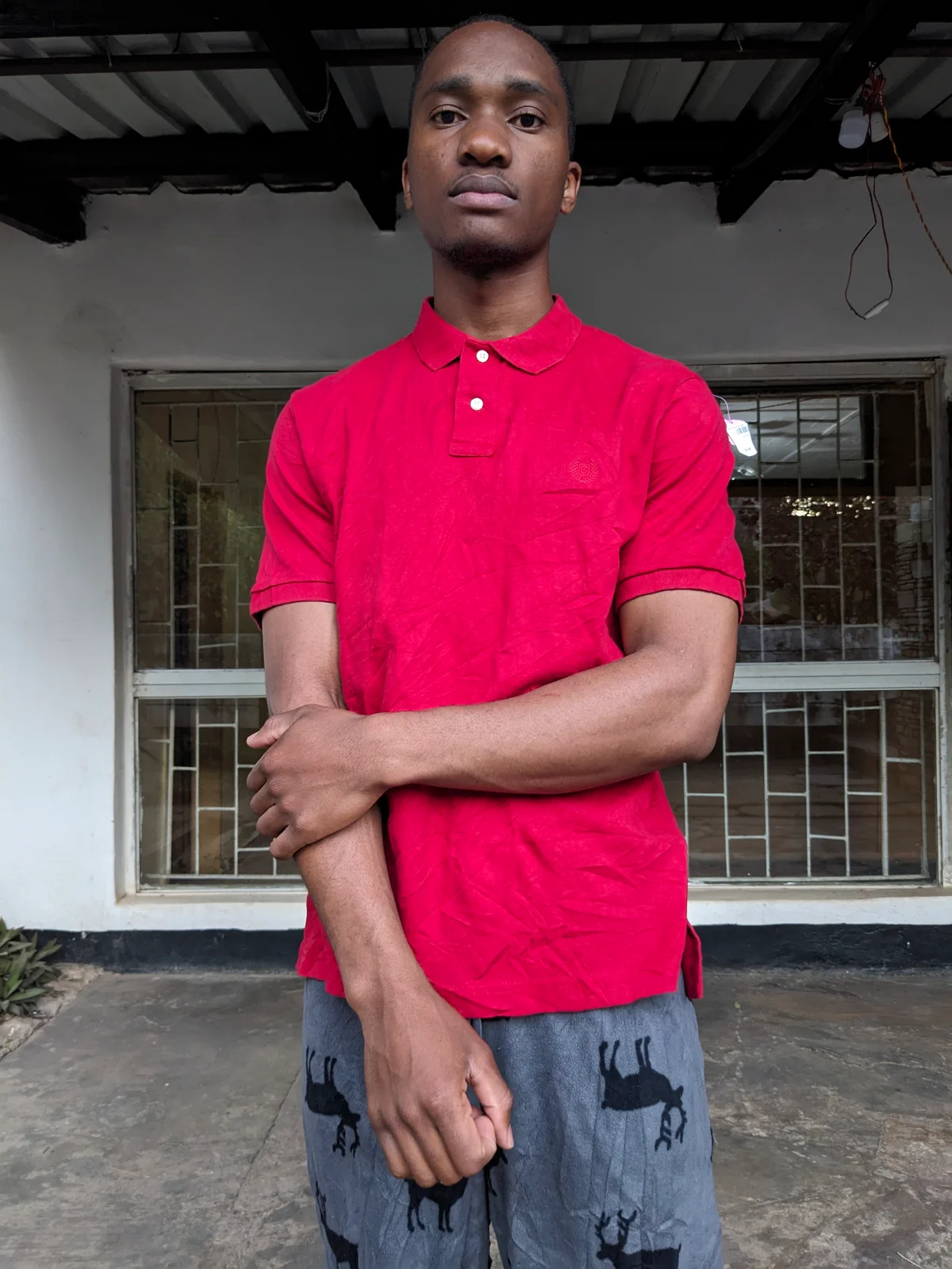 A man wearing a red polo shirt standing in front of a window.