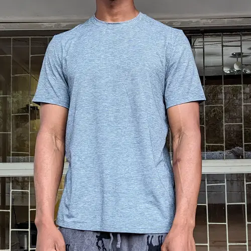 A man wearing a light blue t-shirt and patterned pants standing outdoors.