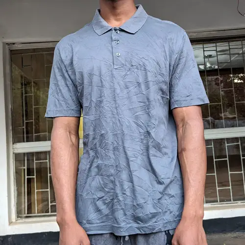 A man wearing a casual blue polo shirt standing outdoors.