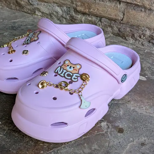 A pair of cute pink clogs with character designs and embellishments.