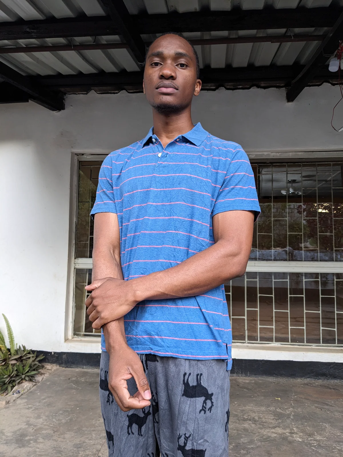 A man wearing a blue polo shirt with pink stripes, standing outdoors.