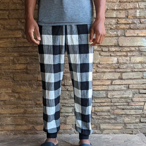 A man wearing checkered lounge pants with a gray shirt.