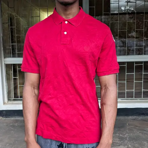 A man wearing a red polo shirt standing in front of a window.