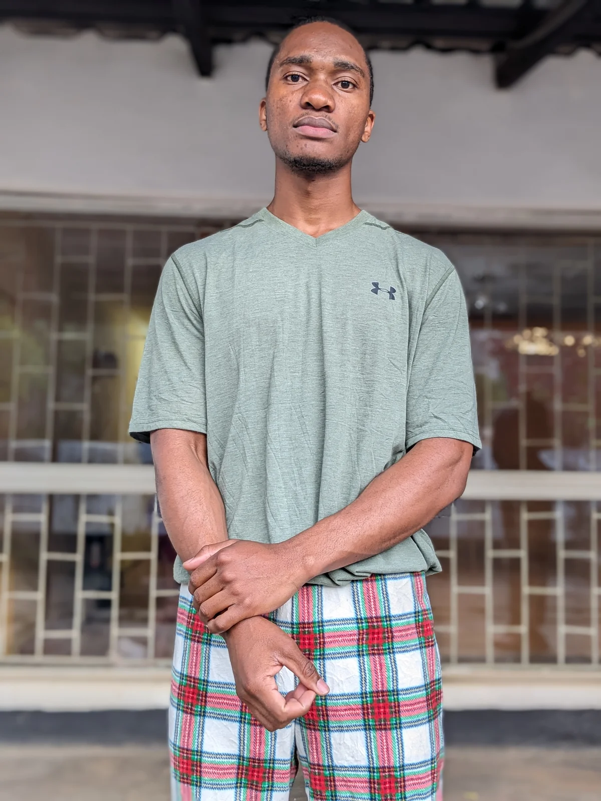 A man wearing a green v-neck t-shirt with plaid shorts.