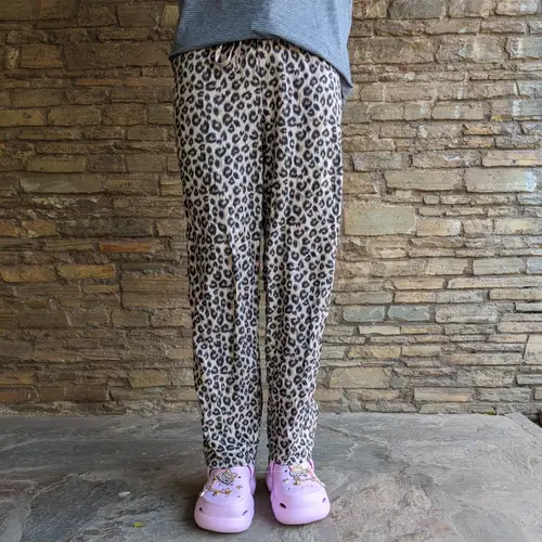 A person wearing leopard print lounge pants and pink shoes.